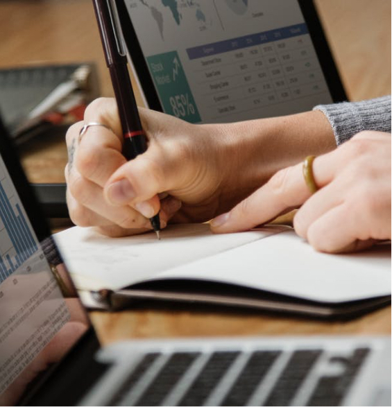 Close up of woman's hand wearing rings and writing in a notebook in front of a laptop